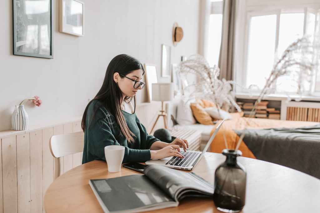 female freelancer typing on laptop while sitting in bedroom