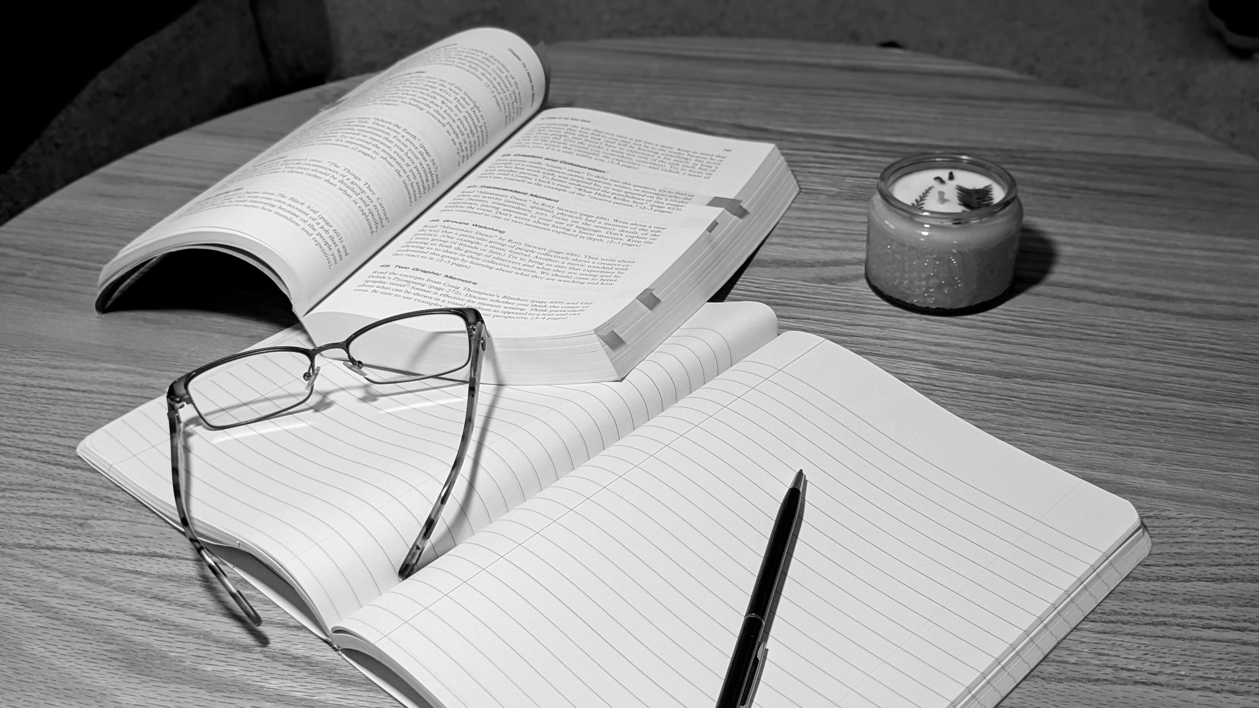 An open book with highlighted and tagged pages next to a notebook opened to a blank page with a pen resting on top.